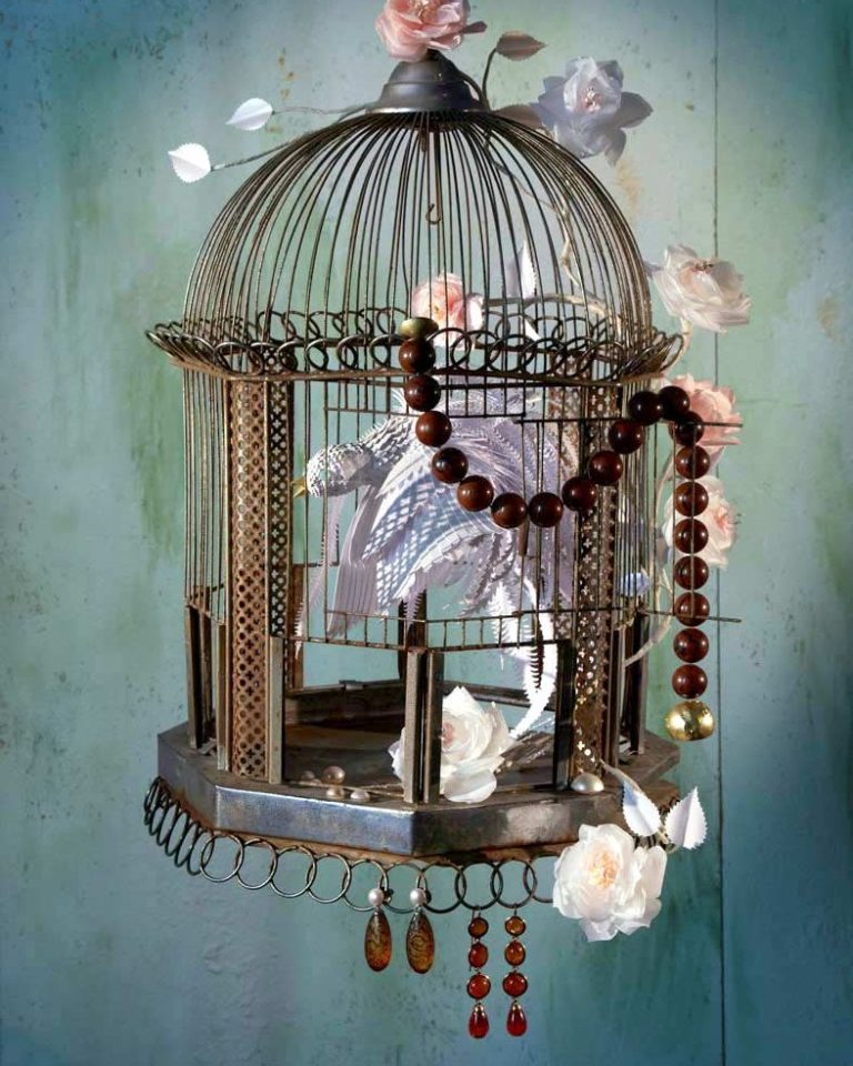 Käfig mit Schmuck behängt und weißem Papiervogel.