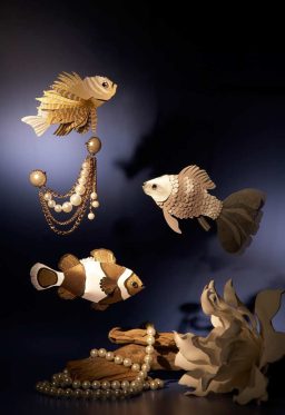 Goldfische aus Papier und Perlenketten auf einem dunklen Hintergrund, künstlerisch arrangiert.