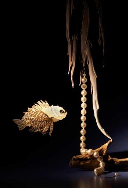 Ein kunstvoll gestalteter Fisch aus Papier schwebt neben einer Schnur aus Muscheln und Pflanzen.