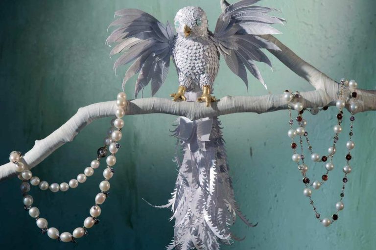 Ein eleganter Vogel aus weißem Papier auf einem Ast, umgeben von Perlenketten.